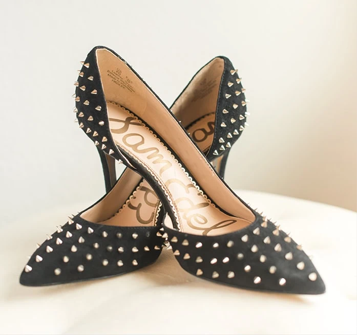 A pair of black pointed toe high heeled shoes covered in small metal studs are crossed over one another.