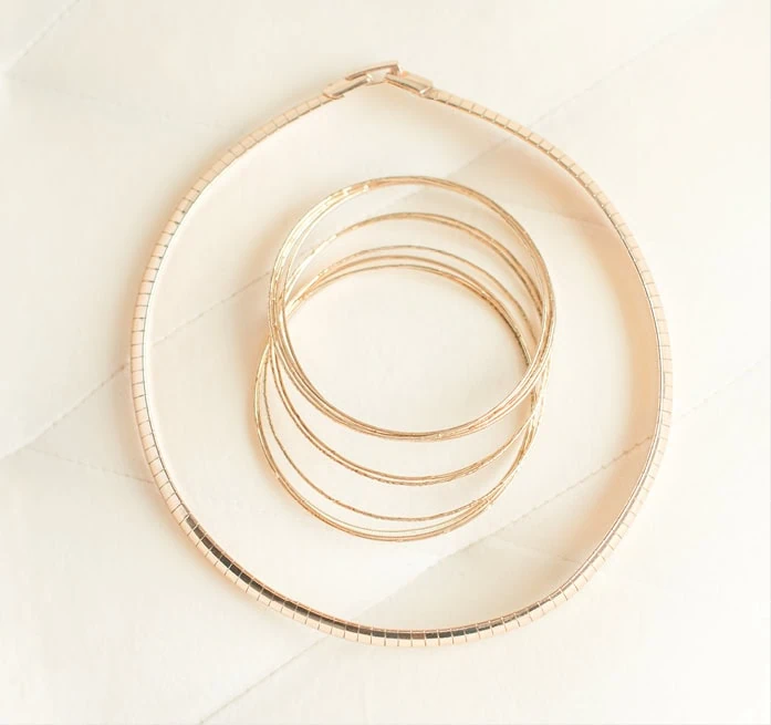 A gold necklace encircles a pile of gold bangle bracelets.