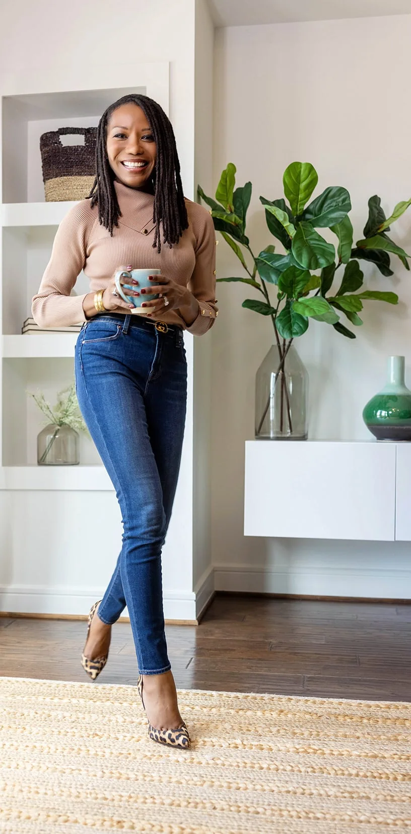 Full-length shot of image consulting expert Roxanne holding a cup of coffee while smiling and being impeccably dressed in leopard print heels, jeans, and a dusty rose sweater.