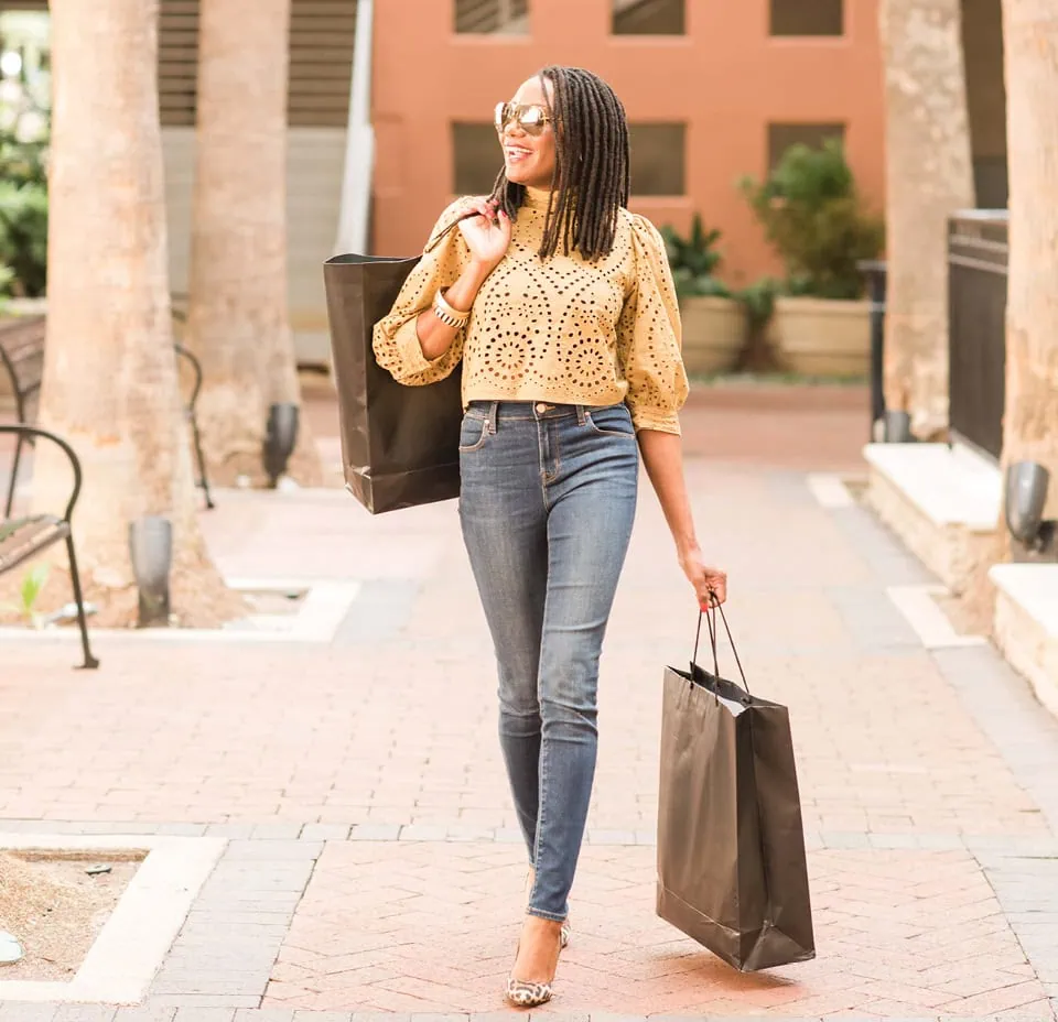 Roxanne Carne, a personal stylist, wearing sunglasses walking on a brick path carrying shopping bags
